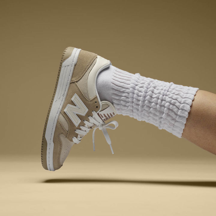 new balance sneaker I beige toner på en fot med hvit sokk på beige bakgrunn